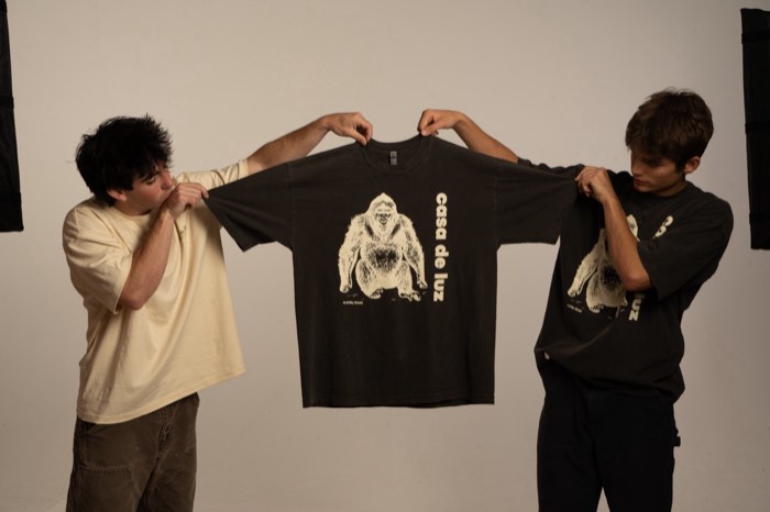Two people holding up a Casa de Luz printed t-shirt during a studio photo shoot